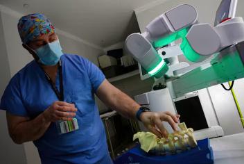 Surgeon in blue scrubs stands in front of glowing robot