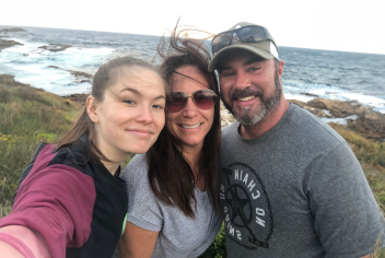 Three people smiling towards the camera with the ocean in the background 