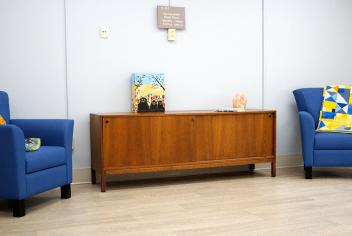Two blue chairs with decorative pillows and a cabinet with a salt lamp sit in a bright room
