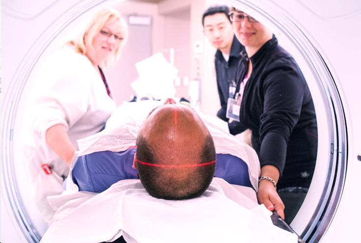A patient lying down in an MRI machine while three nurses talk to him